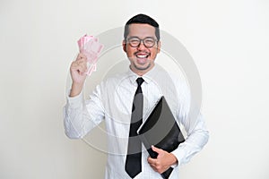 Asian businessman holding a laptop and paper money showing happy expression