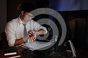 Asian businessman looking clock watch sitting at the desk working late, overtime night working or studying concept