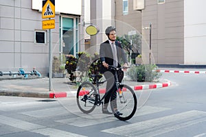 Asian businessman pushes a bicycle across a crosswalk on a city street during a morning commute