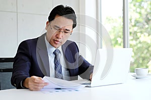 Asian businessman reading papers and working with laptop compute