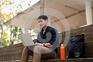 Asian businessman with reusable eco friendly ecological cup using laptop and sitting outside the office building. Eco