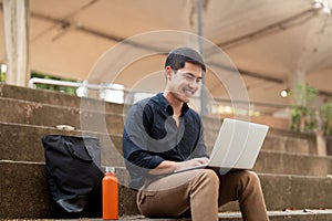 Asian businessman with reusable eco friendly ecological cup using laptop and sitting outside the office building. Eco