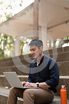 Asian businessman with reusable eco friendly ecological cup using laptop and sitting outside the office building. Eco