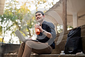 Asian businessman with reusable eco friendly ecological cup using laptop and sitting outside the office building. Eco