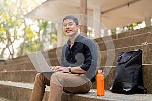 Asian businessman with reusable eco friendly ecological cup using laptop and sitting outside the office building. Eco