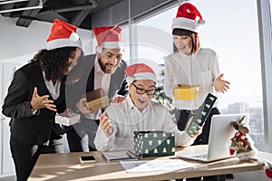 Asian businessman in Santa hat unpacks a Christmas present from multinationals colleagues