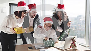 Asian businessman in Santa hat unpacks a Christmas present from multinationals colleagues