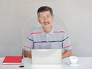 Asian businessman, seniors enjoy using laptops on a white table. With a pen and a red book.He is studying the use of modern