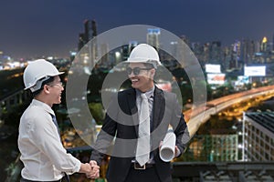 Asian businessman shake hand with engineer architect professional wearing safety helmet and holding construction roll plan for