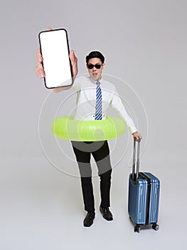 Asian businessman showing smartphone mockup of blank screen holding luggage check-in going to travel on summer holidays isolated