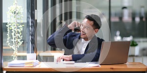 Asian businessman sitting on the phone with a customer with a laptop and document at his office desk.