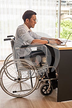 Asian businessman sitting on wheelchair and typing on laptop