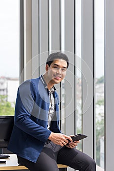 Asian businessman smiles and enjoys the job in a comfortable holding the tablet in the office