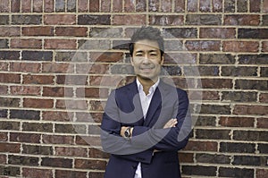 Asian Businessman smiling standing next to the brick wall