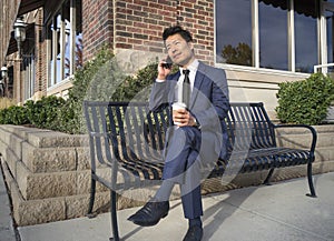 Asian Businessman smiling and talking on the mobile phone on the bench