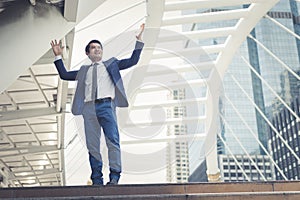 Asian businessman stand and raising up two hands to cheerful and celebrated his successful in career and mission.