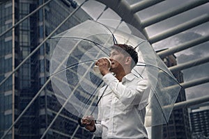 Asian businessman standing and holding a cup of coffee and umbrella during rainy season in city with foreground of faling rain