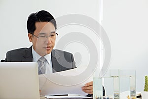 Asian businessman in suit looking at report, personal working with laptop in the office