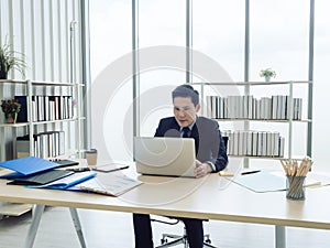 Asian businessman in suit sitting at table and working on laptop computer in office.