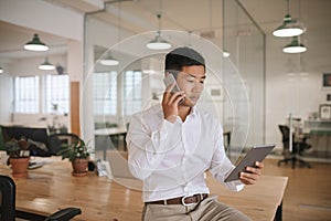 Asian businessman talking on his cellphone and using a tablet