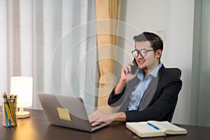 Asian businessman talking on the phone while working on desk with laptop at home