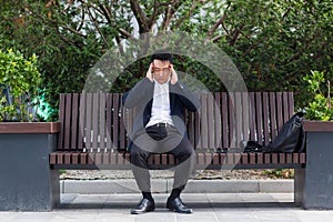 Asian businessman tired after work, sitting on a bench with fatigue and headache, has stress and panic attacks