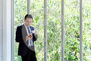 Asian businessman using smart phone and drinking coffee at office, office life and business concept