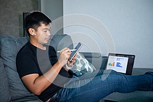 Asian businessman using wireless earphones and using computer notebook and tablet working from home.He is prepare graphs and