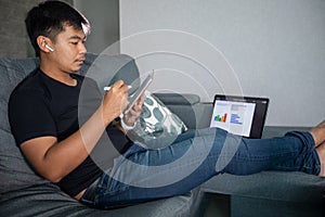 Asian businessman using wireless earphones and using computer notebook and tablet working from home.He is prepare graphs and