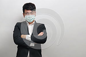 Asian businessman wear face mask and glasses with a white shirt and black suite crossing arms, serious face, look at the camera