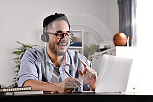 Asian businessman wearing headset on video call with clients on laptop. Young Asian man in glasses giving online educational class