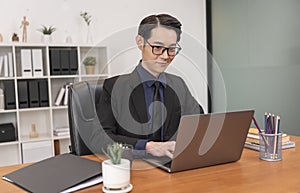 Asian businessman working on laptop in office. Successful Asian business man working on computer while sitting at desk. Smiling