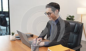 Asian businessman working on laptop in office. Successful Asian business man working on computer while sitting at desk. Smiling