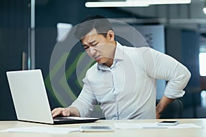 Asian businessman working in office, having severe back pain, overtired worker working with laptop