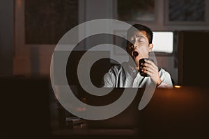 Asian businessman yawning in a dark office late at night