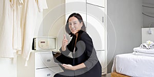 Asian businesswoman in black suit sitting with tablet computer in her hand. The hotel manager verify the tidiness of the room for