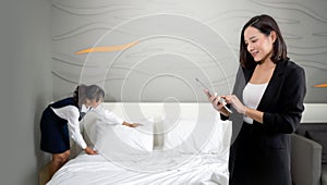 Asian businesswoman in black suit standing with tablet computer in her hand. The hotel manager verify the tidiness of the room for