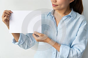 Asian businesswoman in blue shirt holds a blank sheet of paper in hands for advertisement isolated over white background. Copy