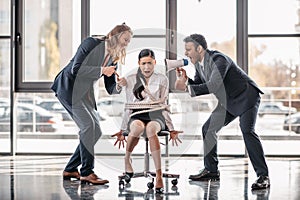 Asian businesswoman bound with rope on chair while businessmen screaming on her with megaphone