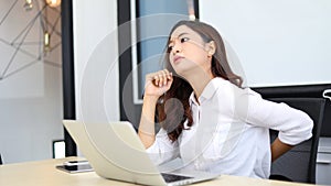 Asian businesswoman feeling aches and pains from work and he is sitting in a chair in her office with a notebook on her desk