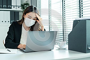 Asian businesswoman in formal suit wear facemask and work at workplace. Attractive female employee office worker feeling sick