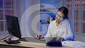 Asian businesswoman or freelancer is busy at work, she talks on the phone and types until overtime at night.