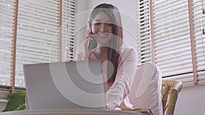 Asian businesswoman on the phone seated at a cafe table, a busy entrepreneur working from afar in a coffee shop with laptop