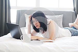Asian businesswoman is relaxing and laying with laptop in bedroom on holiday. She is online working from home with technology