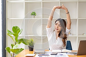 Asian businesswoman relaxing working at desk with graph papers and laptop, mobile phone with calculator in office.