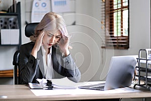 Asian businesswoman are serious at work causing headache stressed out with documents with a laptop at the office.