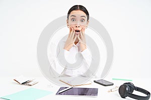 Asian businesswoman with shocked face, looks concerned and overwhelmed at camera, sits in office, white background