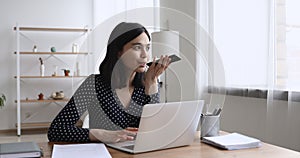 Asian businesswoman sitting at desk speaks with client by speakerphone