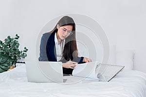 Asian businesswoman sitting and working on white bed
