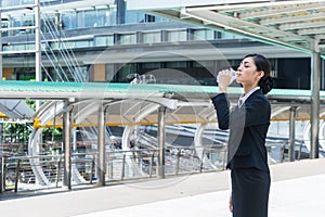 Asian businesswoman standing and drinking pure mineral water from plastic bottle. with copy space